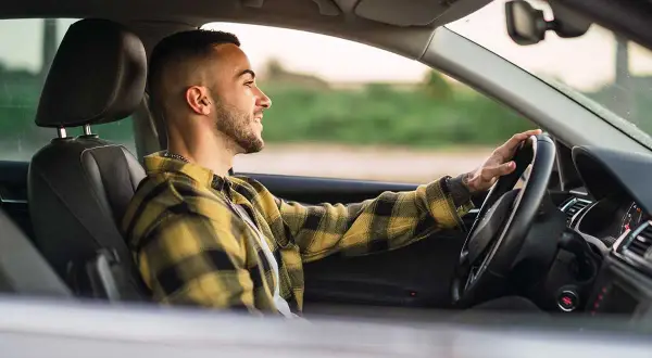 Joven sonriente conduce con las manos en el volante, promoviendo la seguridad al volante.