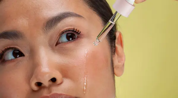 Kropla serum z pipetki spada na policzek kobiety. To może być retinol, który pomaga w pielęgnacji skóry.