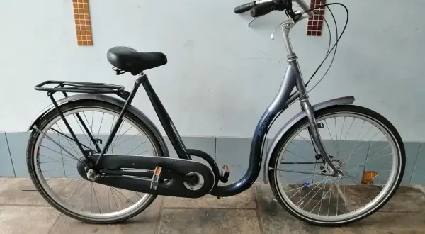 Donkerblauwe cruiser fiets met bagagedrager, geparkeerd voor een muur met mozaïek.
