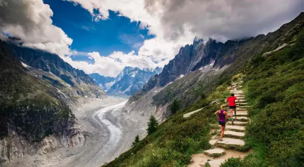 Deux coureurs sur un sentier de montagne escarpé, dominant un glacier spectaculaire. Le **top trail** offre une vue imprenable sur les Alpes.