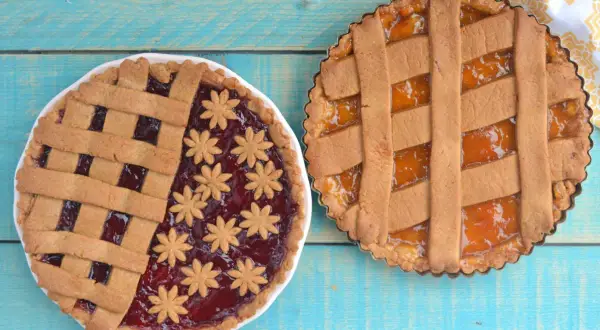 Due crostate senza uova, una con marmellata di frutti rossi e decorazioni a fiore, l'altra con marmellata di albicocche.