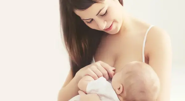 Uśmiechnięta mama karmi piersią dziecko, moment kiedy stabilizacja laktacji przynosi spokój i bliskość.