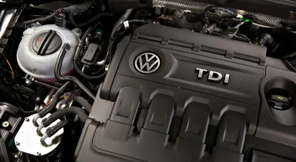 Silnik 2.0 TDI 140KM Volkswagena. Widoczny zbiornik płynu chłodniczego i osłona silnika z logo TDI.