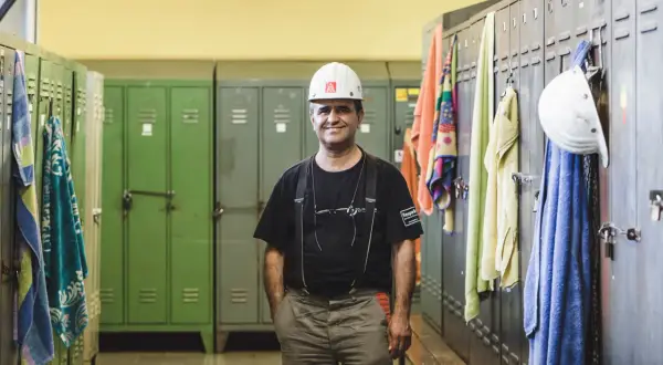 Ein Mann in Arbeitskleidung und Helm steht in einer Umkleidekabine. Handtücher hängen an den Spinden. Die Umziehzeit ist Teil der Arbeitszeit.