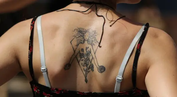 Tatuaz znak zodiaku na plecach kobiety, przedstawiający postać z kwiatami w geometrycznej ramie.
