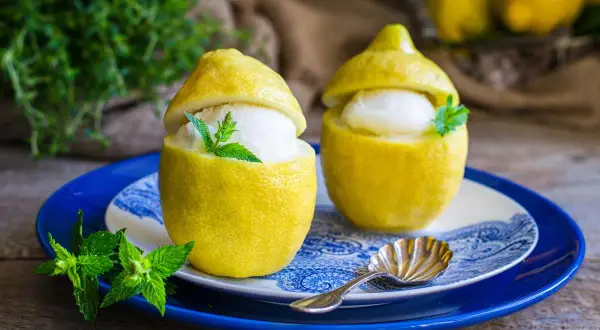 Delizioso gelato al limone servito in limoni svuotati, guarnito con menta fresca. Un'idea rinfrescante preparata con una gelatiera.