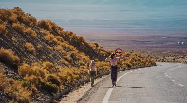 Dwie dziewczynki w kolorowych ubraniach idą pustynią Atacama. Jedna z nich trzyma znak zakazu ruchu.