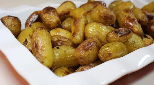Un plat blanc rempli de pommes de terre nouvelles rôties, dorées et appétissantes.