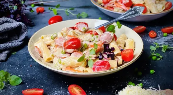 Cremige Pasta mit Würstchen, Erbsen und Kirschtomaten – ein köstliches One-Pot-Gericht, garniert mit frischen Kräutern.