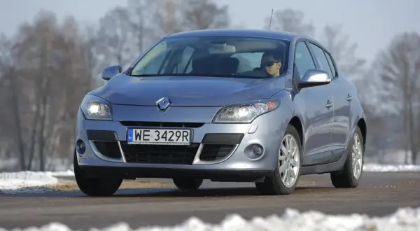 Srebrny Renault Megane 3 z włączonymi żarówkami przód, na drodze zimą.