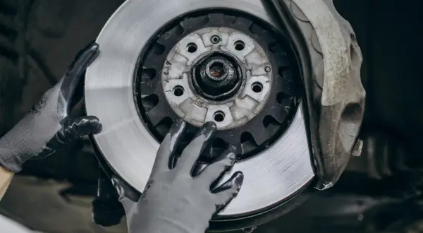 Ręce w rękawiczkach mechanika dokonują wymiany klocków hamulcowych przy tarczy hamulcowej samochodu.