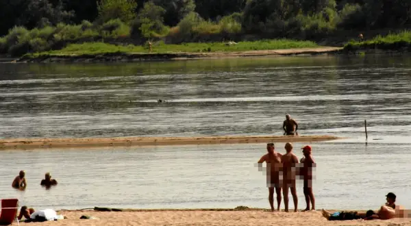 Ludzie opalają się i kąpią na piaszczystej plaży nad rzeką. To popularne miejsce, gdzie można spotkać plażę nudystów.