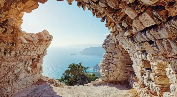Blick durch eine Felsenruine auf das azurblaue Meer. Ein absolutes Rhodos Must See für Geschichts- und Naturliebhaber.
