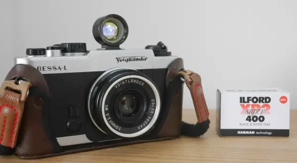 A silver and black Voigtlander Bessa-L camera in a brown leather case sits next to a box of Ilford XP2 Super 400 black and white film.