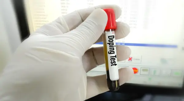 Rękawiczka trzyma probówkę z napisem "Doping Test". Wyniki badań na ekranie sugerują, czy testosteron jest legalny w sporcie.