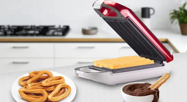 Máquina para hacer churros abierta con churros dentro, plato de churros y tazón de chocolate.