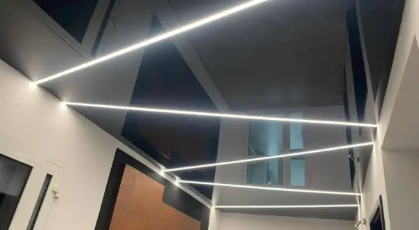 Nowoczesny sufit napinany w salonie z geometrycznymi wzorami i liniowym oświetleniem LED.