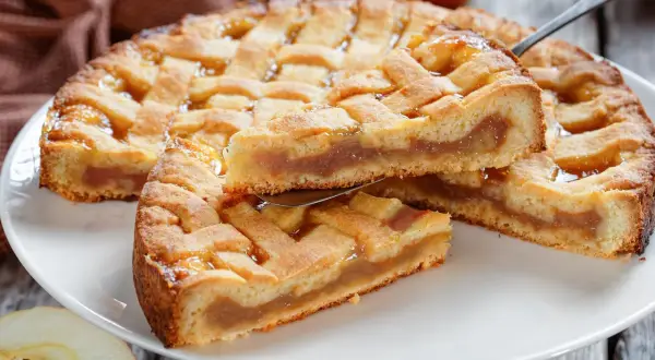 Ein goldbrauner Kuchen mit Gittermuster, gefüllt mit süßem Apfelmus. Ein Stück wird gerade herausgehoben.