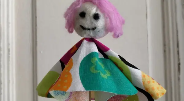 Eine selbstgemachte Puppe mit pinker Wolle als Haar und buntem Stoffkleid. Perfekt zum Filzen mit Kindern.