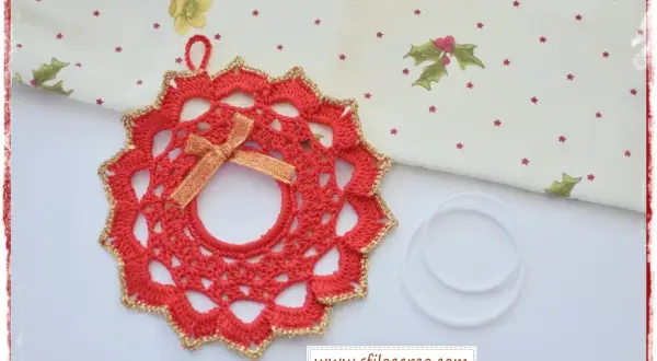 Ghirlanda natalizia uncinetto rossa con bordo dorato e fiocco, pronta per decorare.