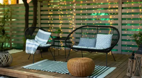 Gemütliche Terrasse gestalten mit wenig Geld: Zwei schwarze Korbsessel, ein Sofa, ein Teppich und Lichterketten schaffen eine einladende Atmosphäre.
