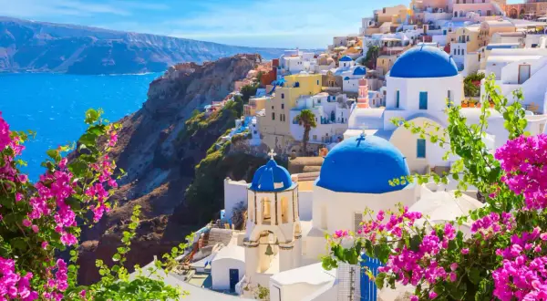 Vue panoramique de Oia, Santorin, l'une des plus belles îles grecques, avec ses dômes bleus iconiques et ses bougainvilliers roses éclatants.