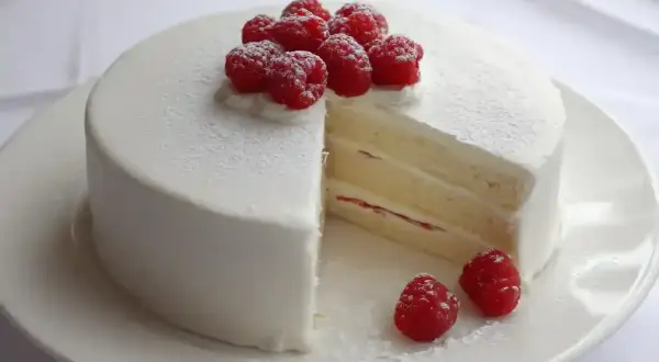 En vacker white lady tårta med fluffig grädde och färska hallon. En bit är bortskuren och visar de läckra lagren.