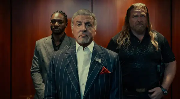 Sylvester Stallone i en serie, flankerad av två män i en hiss.