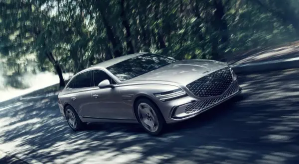 Silver Genesis G80 Sverige glider genom en skogsväg, skuggor dansar över bilen.