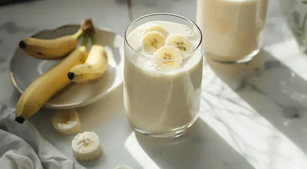 Pyszny koktajl bananowy, ozdobiony plasterkami banana, obok świeżych owoców na talerzyku. Idealny na orzeźwiający początek dnia.