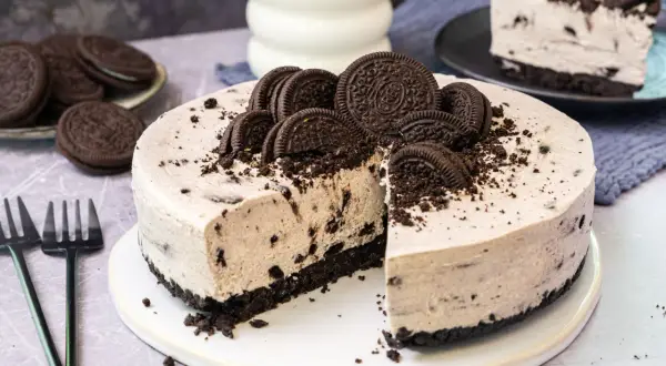 Cremige Oreo Torte mit Biskuitboden, dekoriert mit ganzen und halben Keksen. Ein Stück ist bereits angeschnitten.
