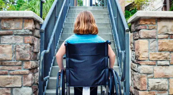 Ragazza in carrozzina affronta una scalinata, un aiuto per l'accessibilità come previsto dalla legge 104.