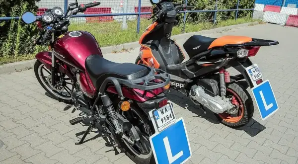 Dwa motorowery z tablicami "L" na parkingu.