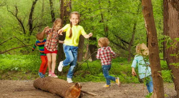 Niños jugando en un tronco, practicando el equilibrio. ¡Una escena de diversión y desarrollo para el equilibrio en niños de 1 a 2 años!