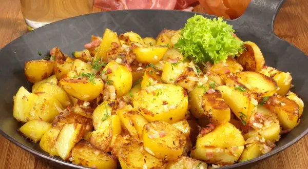 Goldbraune Bratkartoffeln mit Speck und Zwiebeln, garniert mit Petersilie. Ein klassisches Bratkartoffeln Rezept, serviert in einer Eisenpfanne.