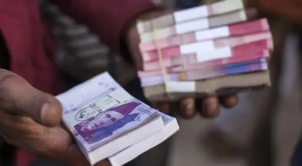 Dłonie trzymają stosy banknotów. W jednej dłoni widać wyraźnie banknot z portretem, to waluta Pakistanu.