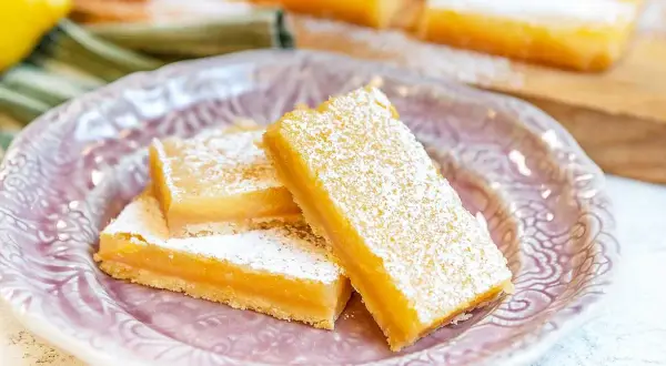 Tre saftiga bitar av citronkaka i långpanna, pudrade med florsocker, ligger på en vacker ljusrosa tallrik.