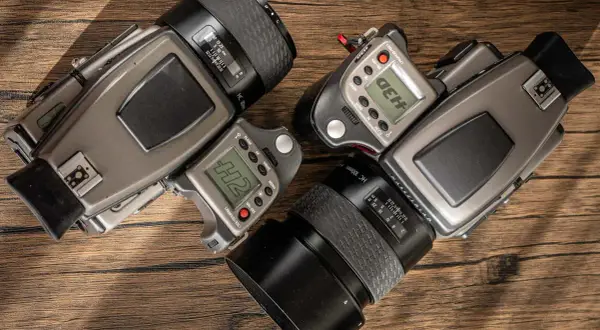 Two Hasselblad H2 camera bodies with lenses and accessories are laid out on a wooden surface.