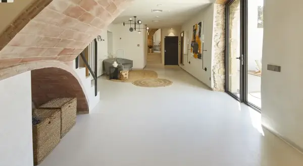Nowoczesny hol z łukiem z cegły, gdzie **mikrocement na płytki** tworzy gładką, jednolitą podłogę. Wnętrze zdobią plecione kosze i abstrakcyjne obrazy.