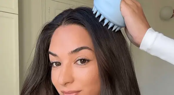 Mujer se masajea el cuero cabelludo con un cepillo azul para evitar cuando se cae mas el pelo.