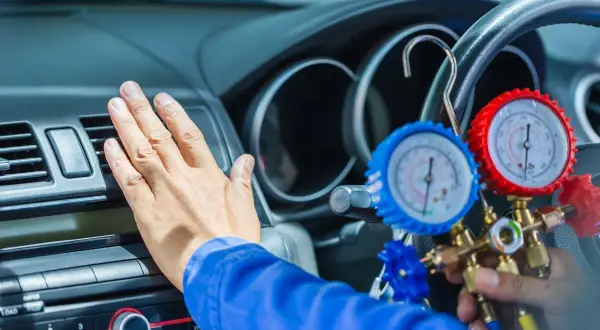 Mechanik sprawdza ciśnienie czynnika chłodniczego w klimatyzacji samochodowej za pomocą manometrów.