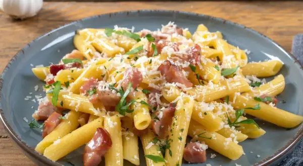 Penne rigate z chrupiącym boczkiem, posypane parmezanem i natką pietruszki. Pyszne makaron z boczkiem na talerzu.