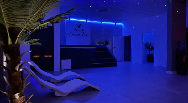 Wnętrze SPA z leżakami, palmą i niebieskim oświetleniem sufitowym.