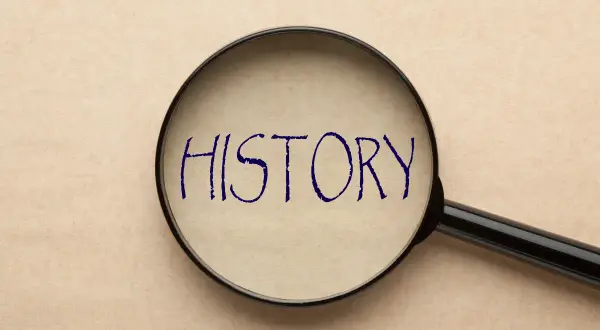 Lupa powiększająca napis "HISTORY" na papierze w kolorze beżowym.