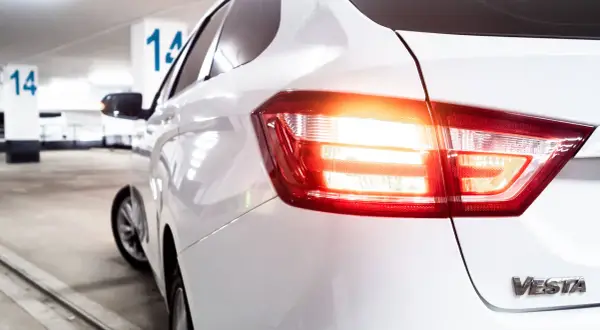 Vue arrière d'une voiture blanche dans un parking. Les feux de recul obligatoires sont allumés, signalant un départ imminent.