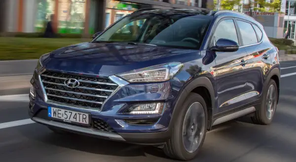 Ciemnoniebieski Hyundai Tucson 2025 w ruchu miejskim, z widocznym grillem i reflektorami.