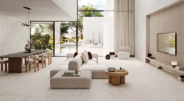 Salon lumineux avec canapé blanc, table à manger en bois et sol en **couleur béton ciré**. Vue sur une piscine et un jardin luxuriant.