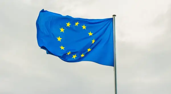 Niebieska flaga z żółtymi gwiazdami, symbolizująca europejski tytuł egzekucyjny, powiewa na maszcie na tle pochmurnego nieba.