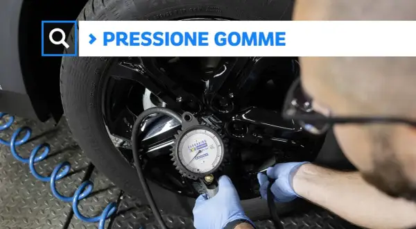 Controllo della pressione gomme auto con manometro. Un tecnico con guanti blu collega lo strumento alla valvola.