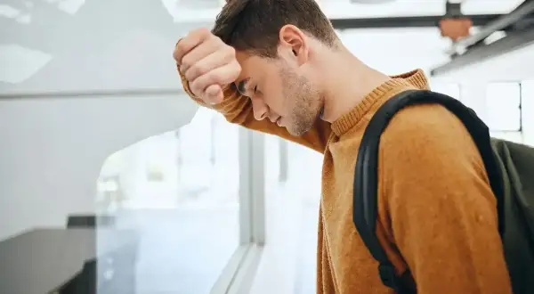 Zmartwiony uczeń z plecakiem opiera się o okno. Czy uczeń nieklasyfikowany jest promowany?
